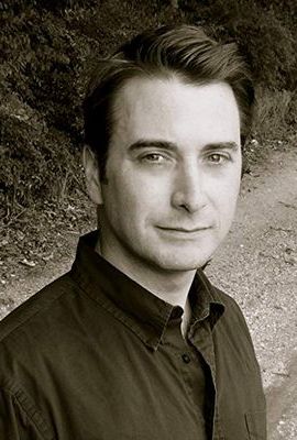 A man in black shirt standing next to a tree.